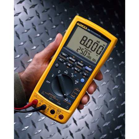 Hand holding Fluke 787 ProcessMeter with active digital display, industrial setting background